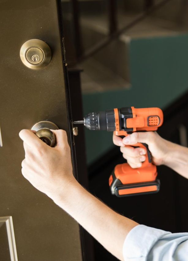 Main sur une poignée de porte et perceuse sans fil en intervention sur la serrure